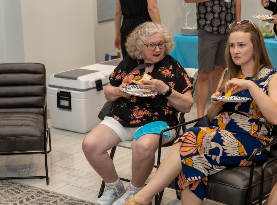 Two women eating food off of paper plates in dental office reception area