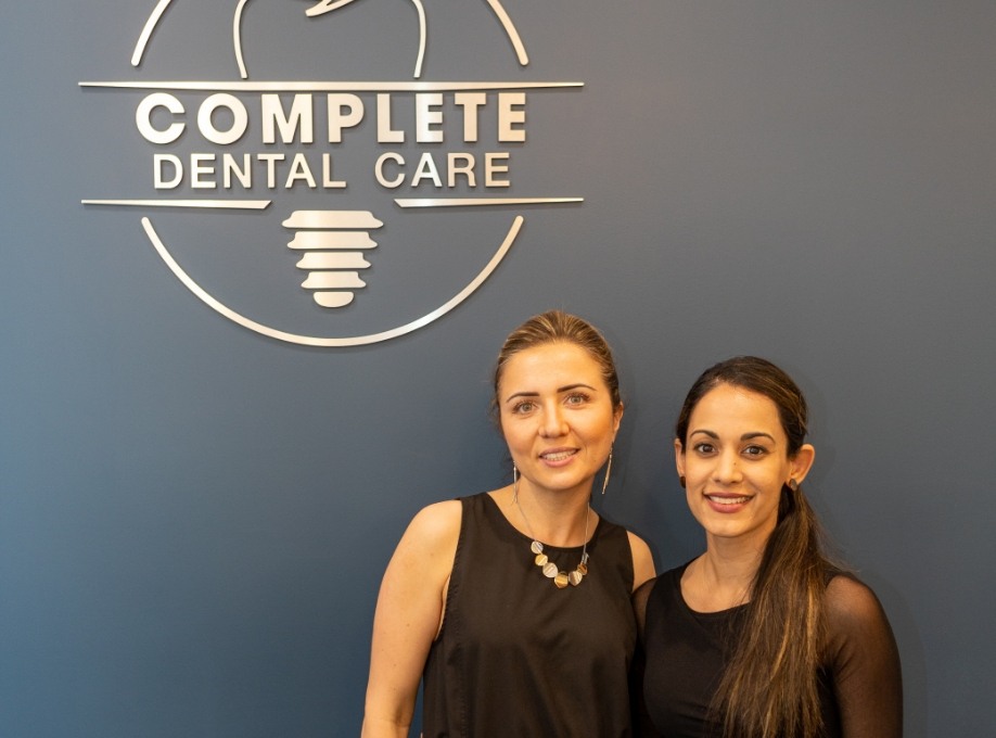 Two women smiling in front of Complete Dental Care Paradise Valley sign on wall
