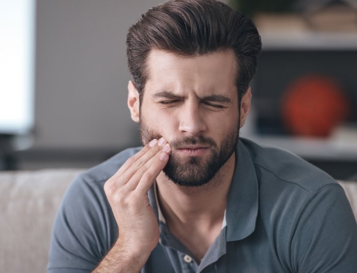 Man in gray polo shirt holding his cheek in pain