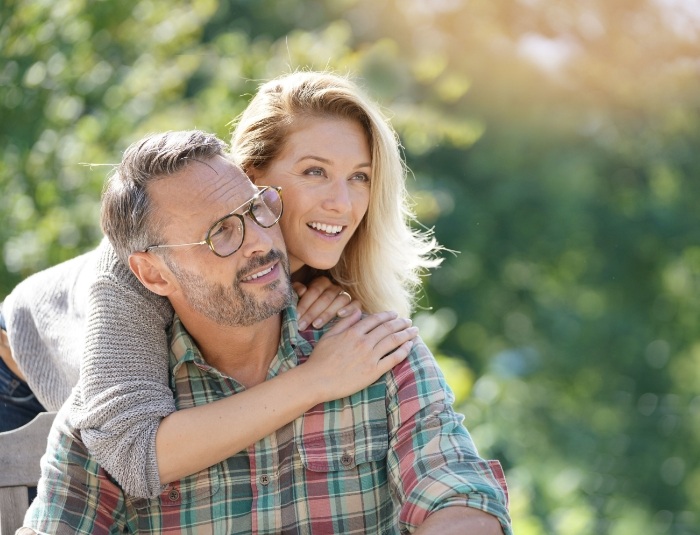 Older man and woman holding each other outdoors on sunny day