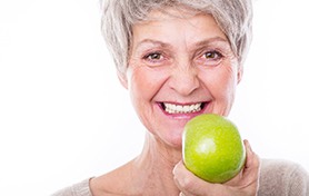 Woman with gray hair holding a green apple in front of her mouth