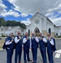 Groomsmen standing in front of a church with their jackets slung over their shoulders