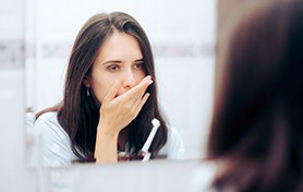 Concerned woman covering her mouth while looking in mirror