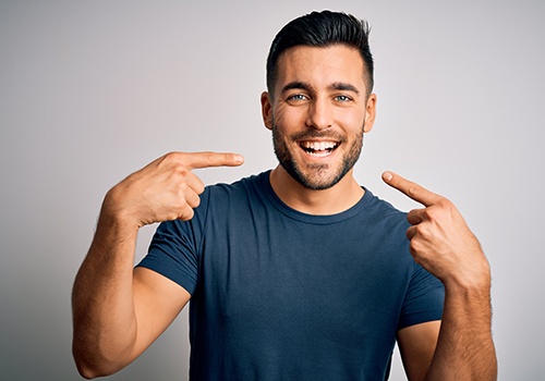 Man in blue shirt pointing to his smile