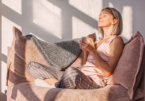 Woman smiling while sitting on couch and drinking tea